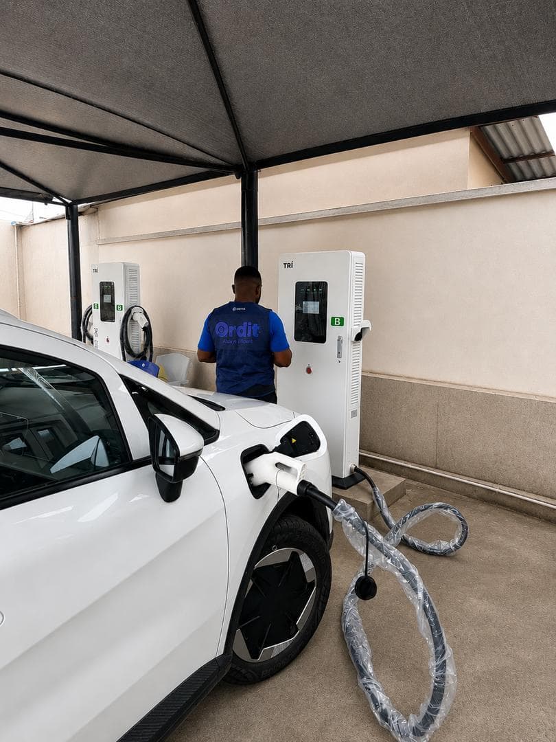 Technician operating a TRI DC fast charger while a white electric vehicle charges at Supersaver, Osapa